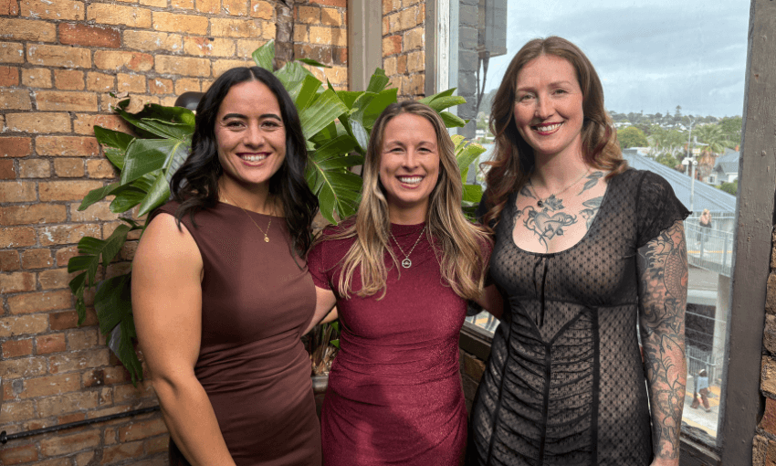 Three women pose for the camera in formal attire. All have long hair and are smiling