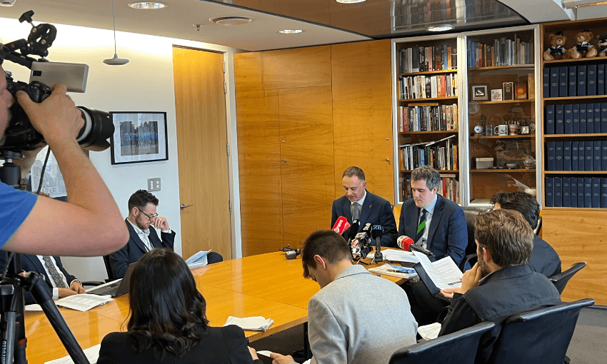 Inside Chris Bishop's office, with Bishop and minister Simon Watts sitting at the head of a table filled with journalists.