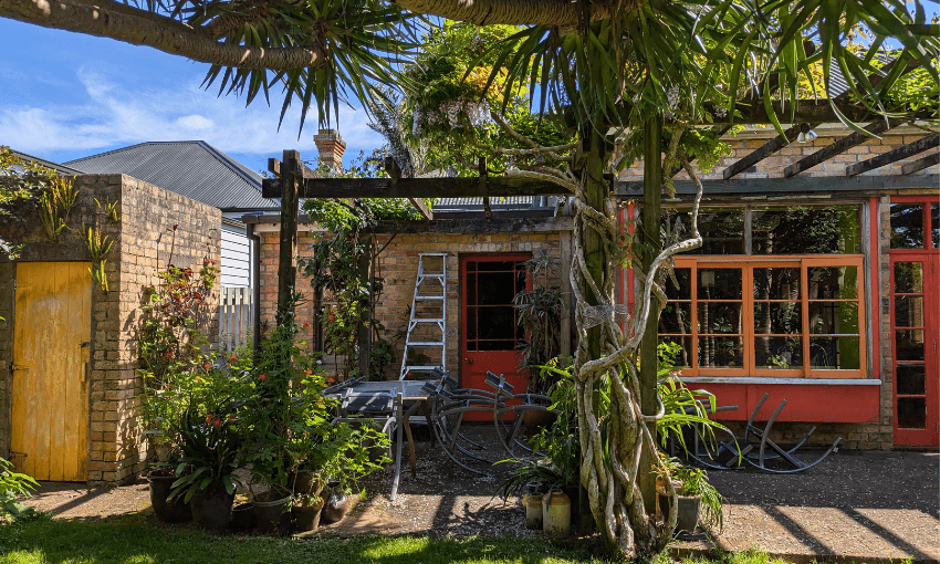 A single storey brick home with a pergola in front of the entrance and red and orange doors and windows