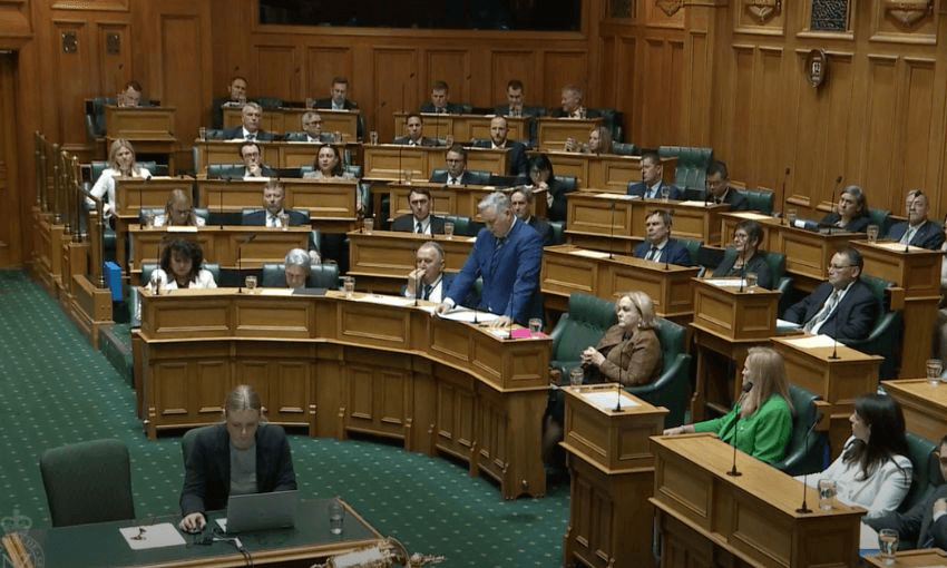 A wide shot of the government benches in the House, showing Mark Mitchell standing and speaking at his desk.