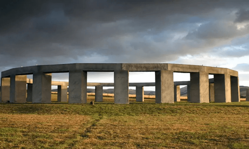 A large outdoor stone sculpture sitting on grass with a gloomy sky above.