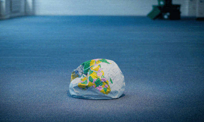 A deflated inflatable globe sits on a blue carpeted floor in an empty room, with some blurred green furniture in the distant background.