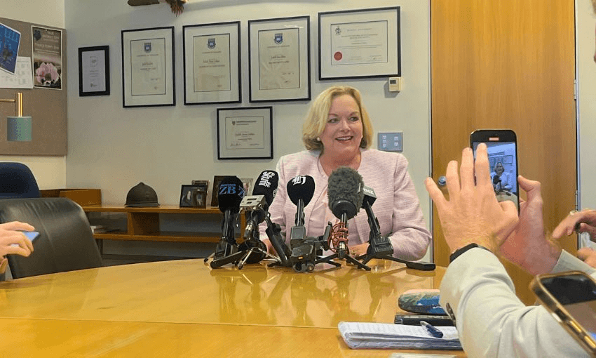 Judith Collins smiles while seated at a top of a long table.