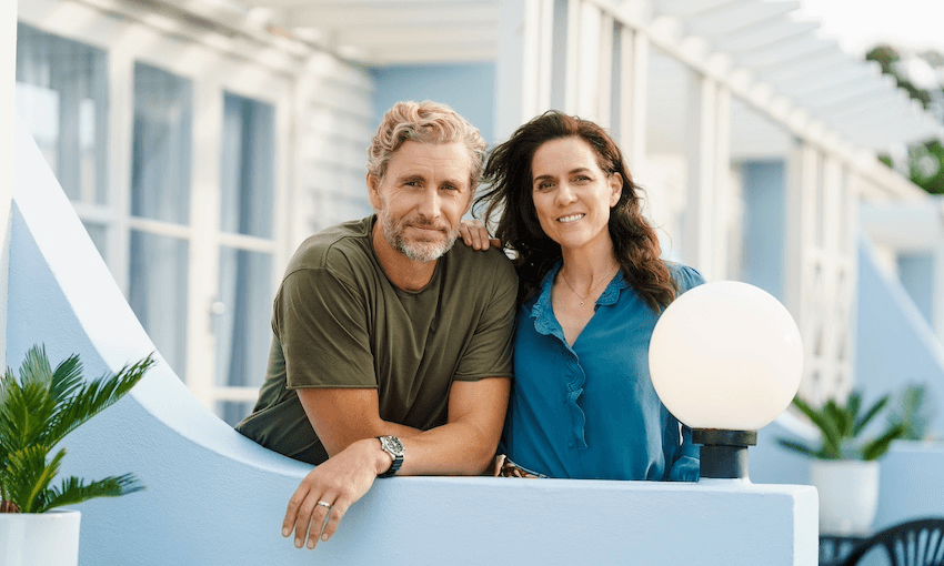 A blonde man wearing a green shirt and a woman with long brown hair and a teal coloured shop smile at the camera