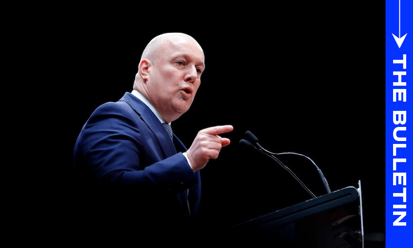 A man in a suit speaks emphatically at a podium, pointing forward. The background is black and a vertical blue banner on the right reads "THE BULLETIN.