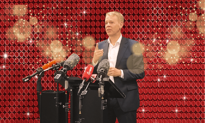 A man in a suit speaks at a podium with several microphones in front of a sparkling, red, circular-patterned backdrop.