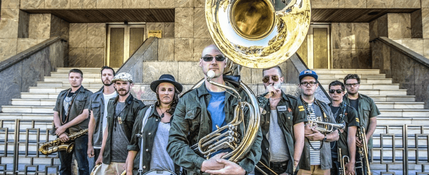 A photograph of a large brass band standing on the steps of a large building and all staring into the camera with serious expressions.