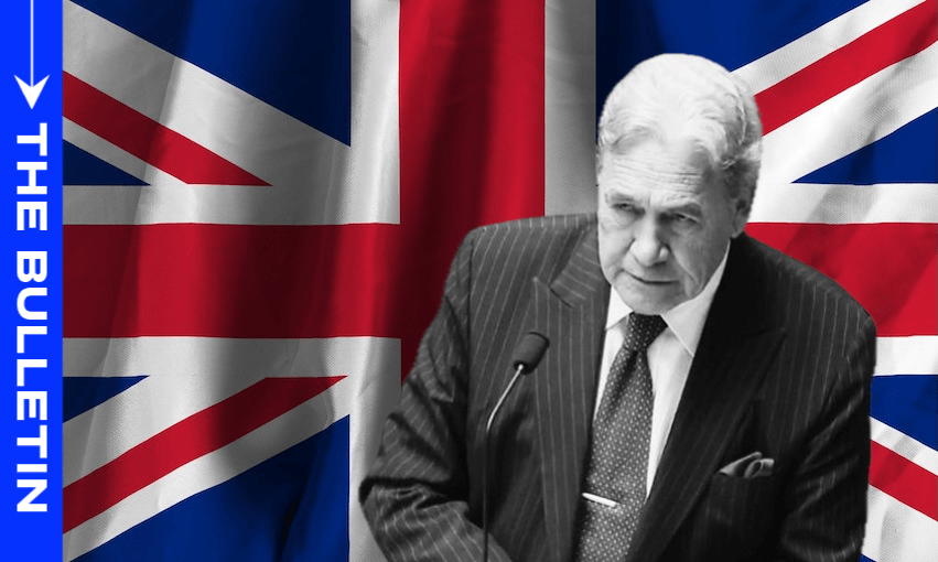 A man in a suit speaks at a podium in front of a large British flag; the left side has a blue vertical banner with the words "THE BULLETIN" in white text.