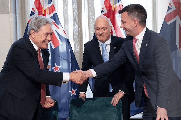 Winston Peters and David Seymour shake hands at the coalition signing ceremony as Christopher Luxon looks on (Photo: Marty Melville / AFP via Getty Images) 
