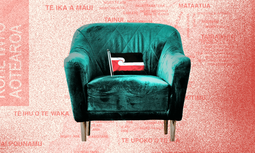 A green, velvet armchair with a small black, red, and white flag sits against a pink background covered in red text in te reo Māori.