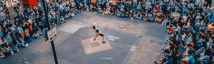 A photograph taken from high up looking over a street performer with a large crowd encircling them.