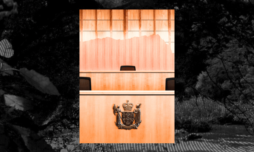 A wooden judge’s bench with an empty chair and a coat of arms emblem is seen in a courtroom, set against a backdrop of wooden paneling and windows.