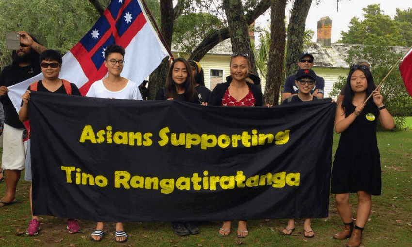 A group of people stand outdoors holding a black banner that reads