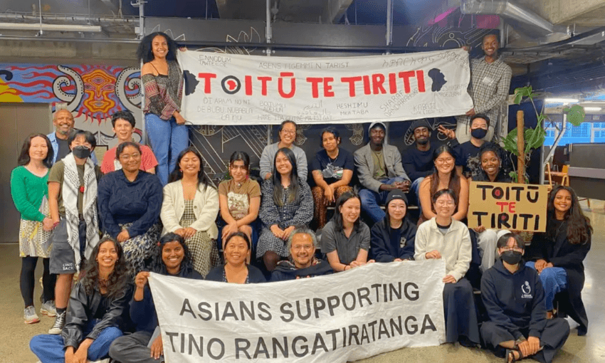 A diverse group of people pose indoors holding signs that read