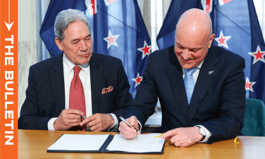 Two men in suits sit at a table with a document; one signs while the other watches. New Zealand flags are in the background. An orange sidebar on the left reads "THE BULLETIN.