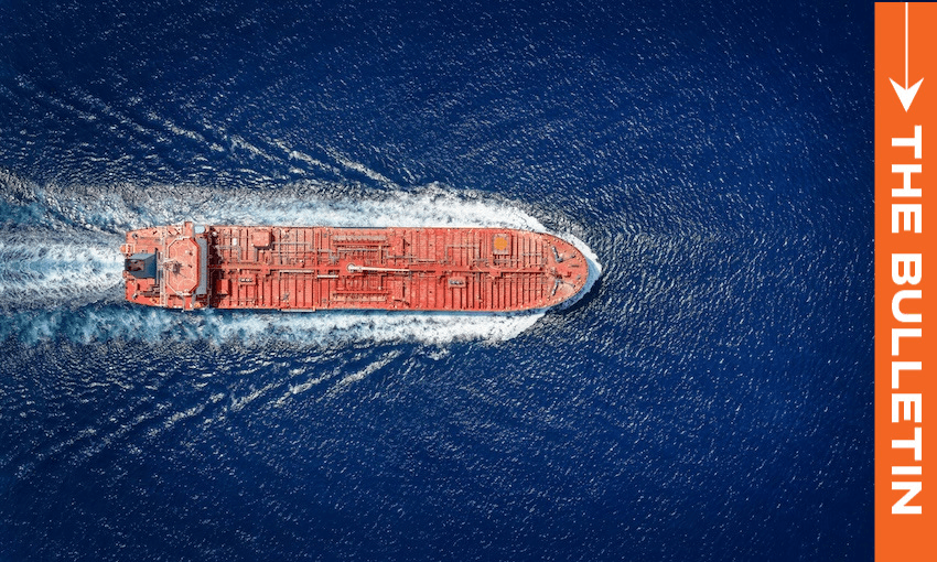 Aerial view of a large red cargo ship moving through deep blue ocean water, creating a white wake. An orange vertical banner on the right reads "THE BULLETIN" with a white arrow above the text.