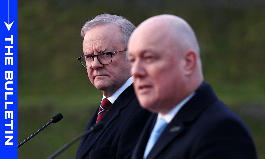 Two men in suits stand at microphones outdoors. The man on the left, wearing glasses, looks intently at the man on the right, who is speaking. A blue vertical sidebar on the left reads "THE BULLETIN.