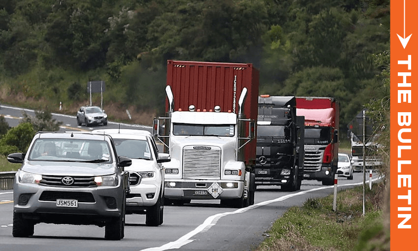 Cars and large trucks drive along a curved, two-lane highway surrounded by greenery, with an orange vertical banner on the right side reading "THE BULLETIN.