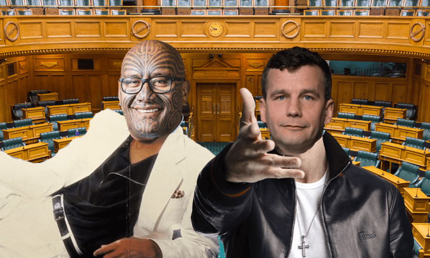 Two men pose in front of empty wooden parliamentary chamber seats; one wears a white suit and glasses with facial tattoos, the other wears a black jacket and gestures with his hand.