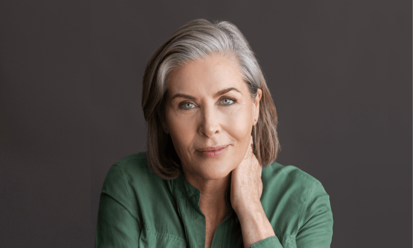 a woman with brown and grey shoulder length hair stares into the camera wearing a dark green collared shirt