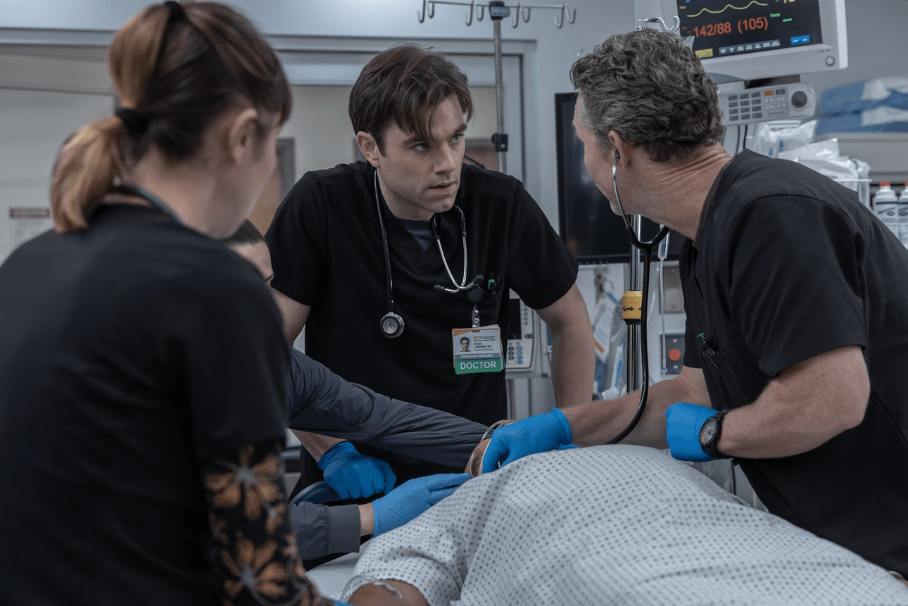 three doctos in black scrubs stand over a prone patient in an emergency department