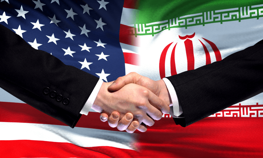 Two people in business suits shake hands in front of blended American and Iranian flags, symbolizing diplomacy or an agreement between the United States and Iran.