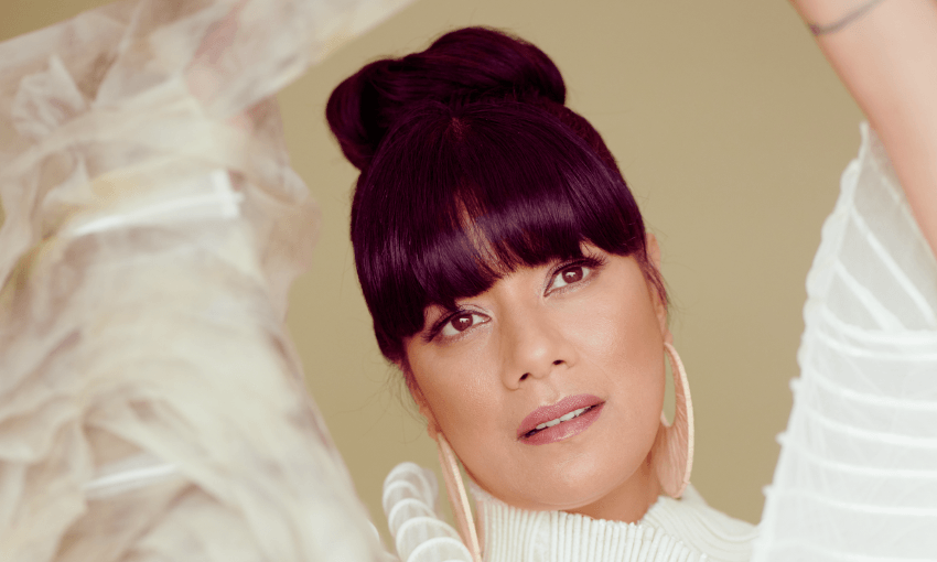 a close up portrait of a woman with black bangs and wearing her hair in a bun, large gold hoop earrings and a flowing cream dress