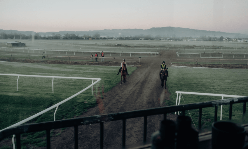 A beautiful sunrise photo from the stands of a racecourse looking out over the track where two horses are being ridden.