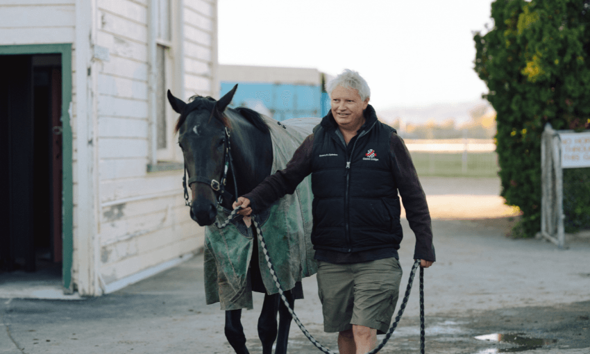 A photograph of a man walking a horse through a racecourse yard.