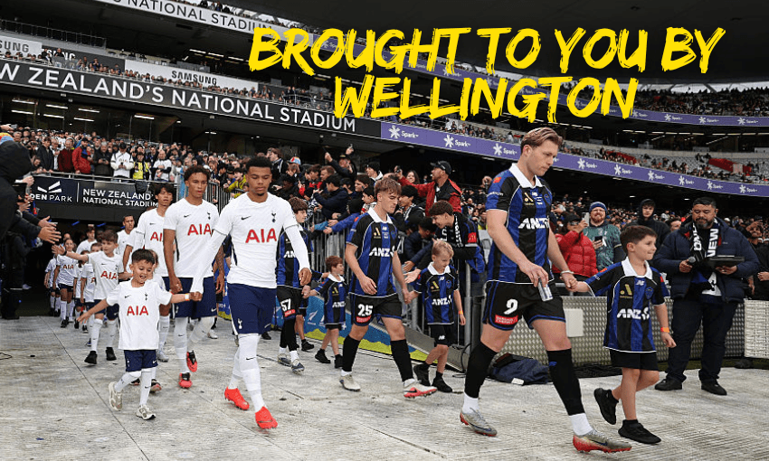 male football players in blue and black, and white uniforms walk onto the field at eden park with a large crowd in the background