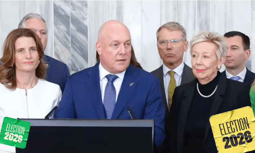 A man in a blue suit speaks at a podium surrounded by people in business attire. The background is marbled. Green and yellow “Election 2023” graphics are in the bottom corners.