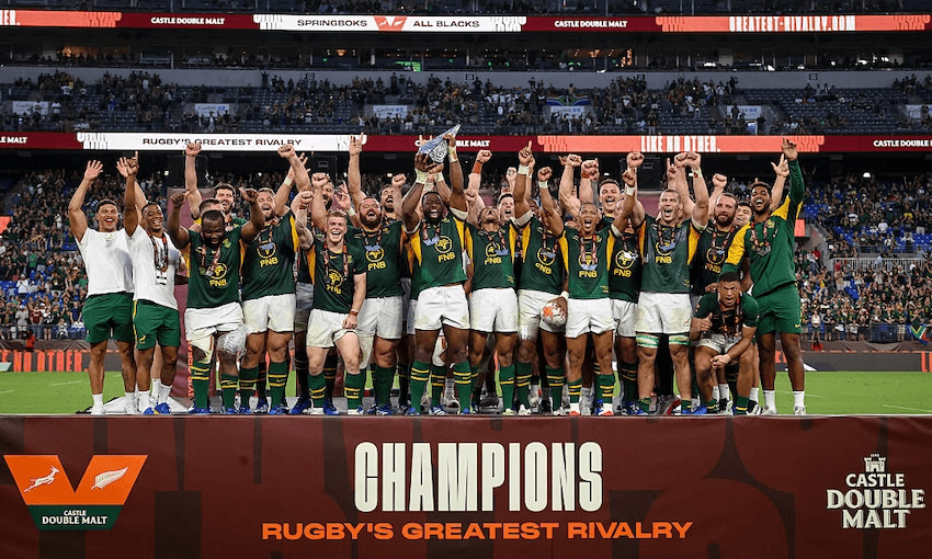 a large rugby team of 30 players wearing green tops and white shorts celebrate with fists raised while standing on a large platform saying "champions"