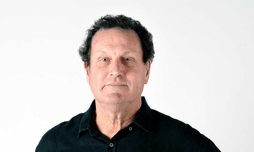 a portrait of a middle aged man with blue eyes, white skin, and dark brown short curly hair. He wears a forest green collared shirt