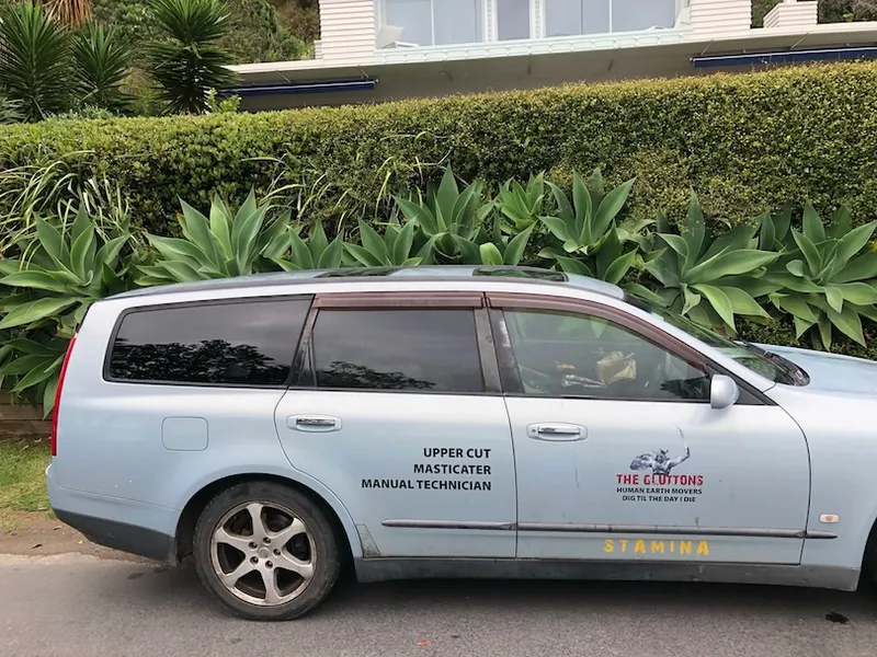 A blue station wagon parked by the road, with text on the door reading “UPPER CUT MASTICTER MANUAL TECHNICIAN” and “THE GLUTTOS” along with a logo and the word “STAMINA” on the side skirt.