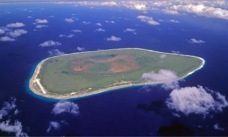 Aerial view of a green island surrounded by deep blue ocean, with some white clouds above and a thin sandy shoreline encircling the island.