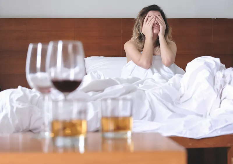 Young exhausted wasted woman waking up suffering headache and hangover after drinking alcohol lying on bed sick and miserable still drunk