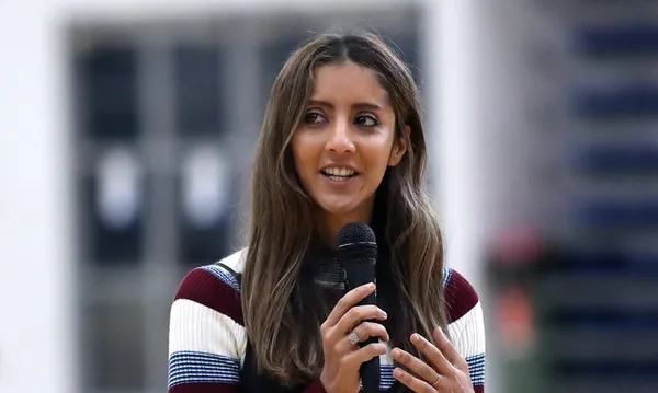 a woman wearing a striped top with long hair medium brown skin and holding a microphone