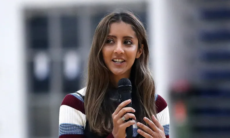 a woman wearing a striped top with long hair medium brown skin and holding a microphone