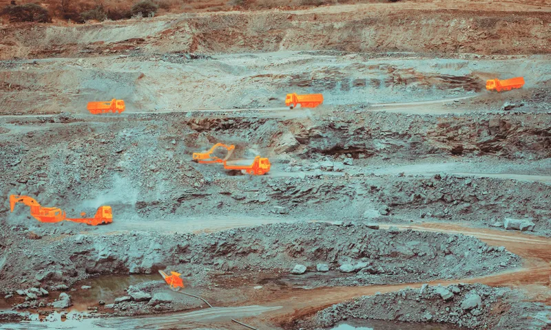 A quarry site with several large trucks and excavators conducting mining operations. The machinery and roads are highlighted in bright orange against the rocky terrain. The area shows layers of earth being excavated.