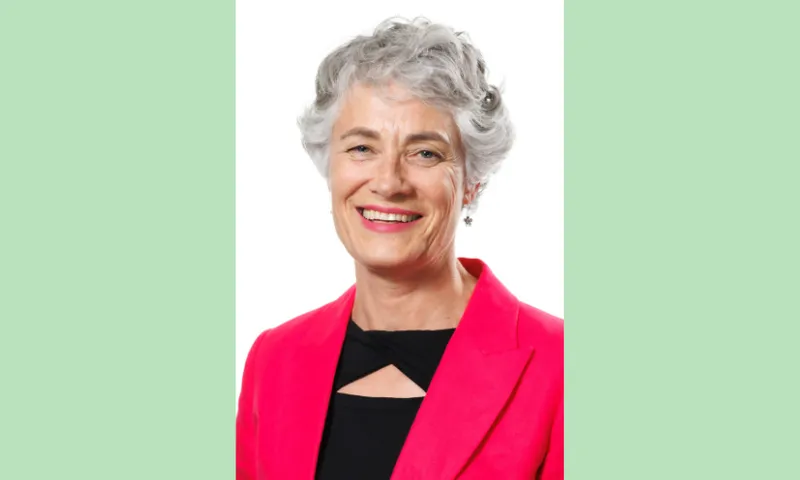 a green background with a photo of Nic Quilty, an older pakeha woman with a pink blazer, black top, curly grey hair and a big smile