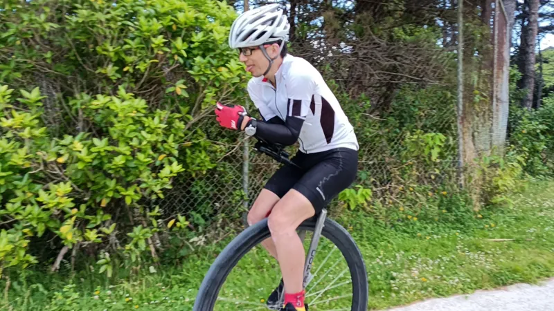 Ken Looi riding his unicycle at Newlands Intermediate during his world record attempt. There are trees in the background. He is poking his tongue out.