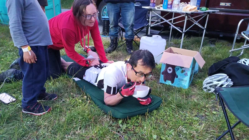 Ken Looi lying down on a cushion during his world record attempt. He is heading a bowl of noodles and his wife is giving him a massage.