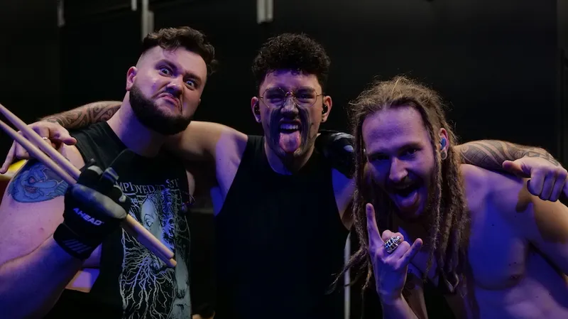 Three members of Alien Weaponry stand on stage doing pūkana and devil horns with their hands