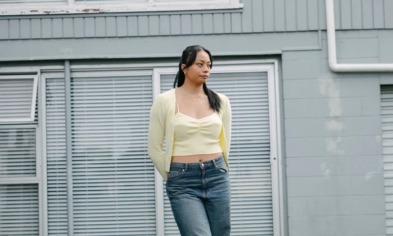 Symone Tafuna’i standing front of a grey house wearing a yellow top