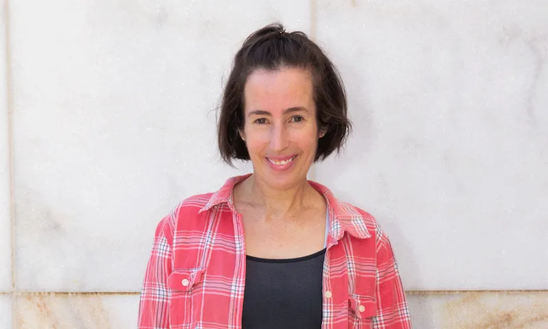A head and shoulders image of Felicity smiling directly into camera in front of a marbled stone wall.