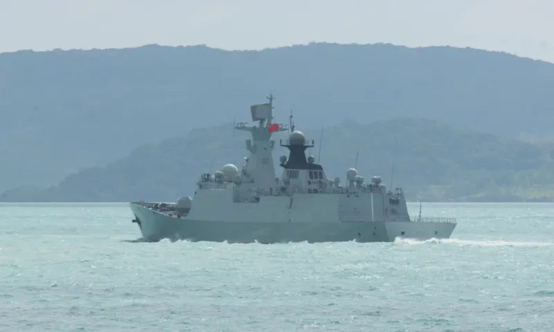 some hazy hills in the background with a grey naval ship on the water