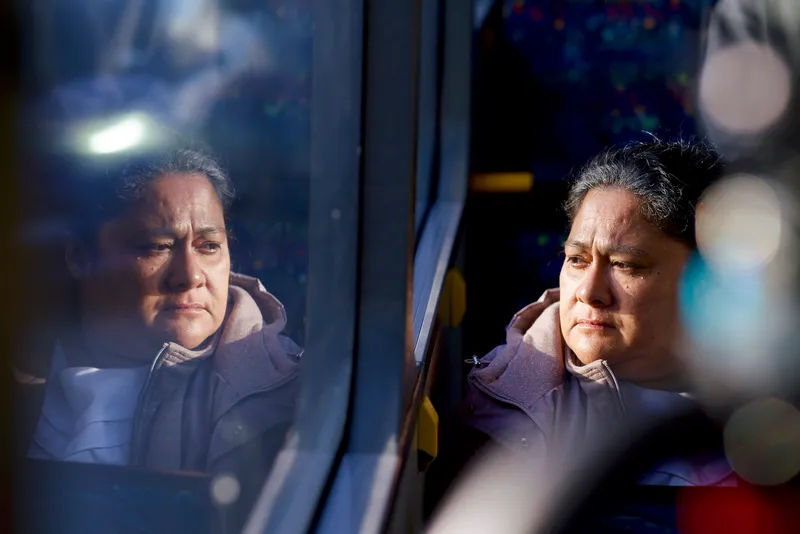 Anapela Polataivao as Tinā in the film Tinā, looking out a bus window with her face reflected in the glass
