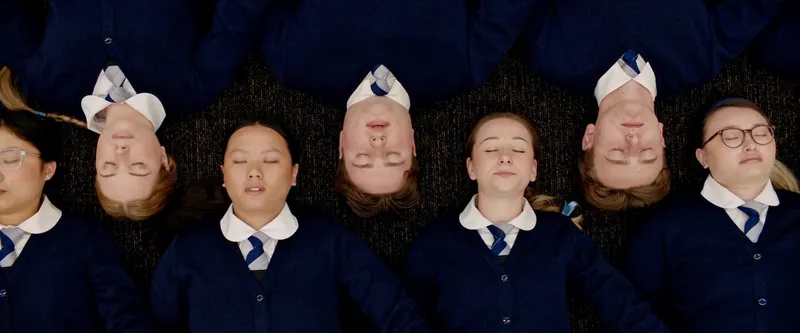 A still from Tinā showing seven school students lying down with their heads alongside each other