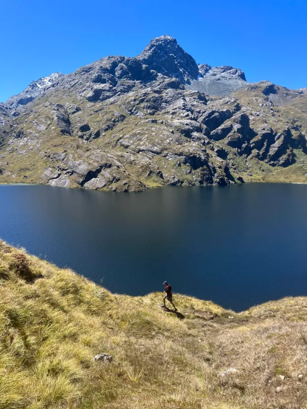 a mountain and lake with small figure hiking along the trail
