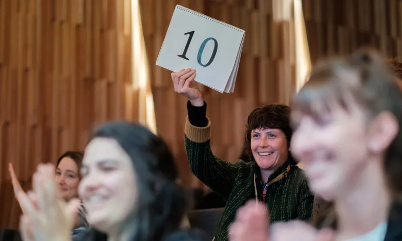 A photo of a crowd. One woman is holding up a sign that says the number 10. She is smiling.